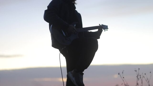 man plays electric guitar gloomily outdoors in cloudy weather
