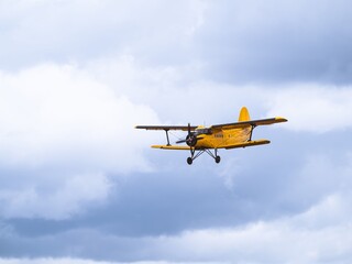 A yellow vintage biplane captured mid-flight against a vast cloudy sky. The classic aircraft's front view showcases its wingspan and intricate details.