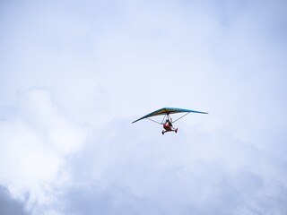A small ultralight trike aircraft soaring in the sky with a pilot. The lightweight aviation design highlights recreational flying and personal air travel against a cloudy backdrop.