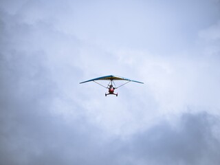 A small ultralight trike aircraft soaring in the sky with a pilot. The lightweight aviation design highlights recreational flying and personal air travel against a cloudy backdrop.