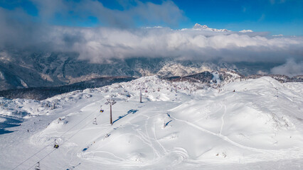 Aerial view of Vogel Ski Resort in Slovenia during winter with blanket of snow covers the slopes and ski lifts in the alpine landscape. Features the striking peaks of Orlove and Pick Sija