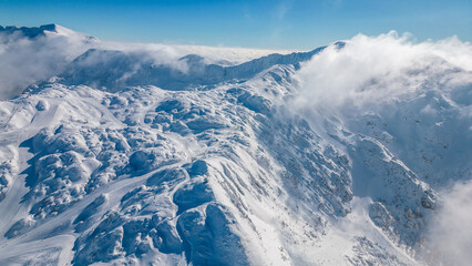 Aerial view of Vogel Ski Resort in Slovenia during winter with blanket of snow covers the slopes and ski lifts in the alpine landscape.  Features the striking peaks of Orlove and Pick Sija