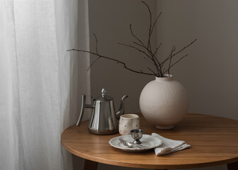 Breakfast is served with a coffee pot - a plate, a glass, a vase with decor on a round wooden table