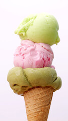 Close-up of a triple scoop ice cream cone featuring green pink and light green flavors against a clean white background.