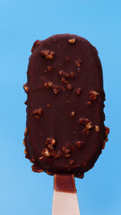 Delicious chocolate-covered ice cream bar with crunchy nut pieces on a wooden stick, set against a vibrant blue background.