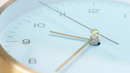 close-up of a modern wall clock with a light blue face and gold-toned hands.