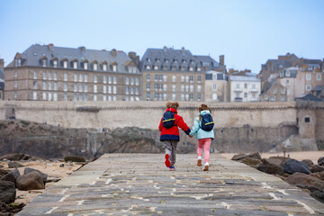 Happy children run on stone path by the sea at tide, Saint-Malo
