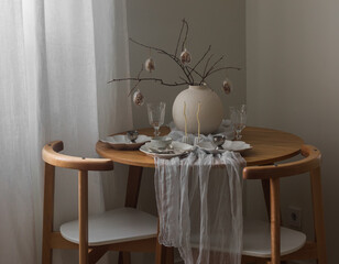 Festive Easter setting - Easter bouquet in a ceramic vase, dishes on a round wooden table in the living room