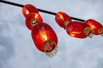 Vibrant red Chinese lanterns hang against a soft, cloudy sky, illuminating the spirit of...