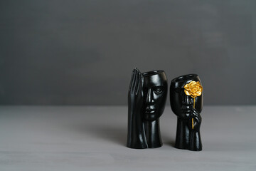 Two black plaster cups shaped as male and female faces on a gray background. Minimalist and creative concept for design, art, or office themes.