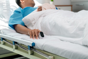 Asian patient lying in hospital bed, wearing pulse oximeter, demonstrating medical monitoring and patient care in clinical healthcare environment