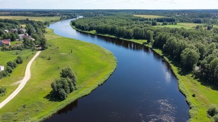 Obraz premium Aerial view of a meandering river flowing through a green landscape, with houses visible in the distance under a partly cloudy summer sky. The dark