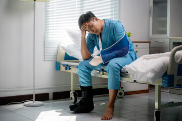 Young asian patient wearing blue hospital uniform, sitting on bed, experiencing pain from broken...