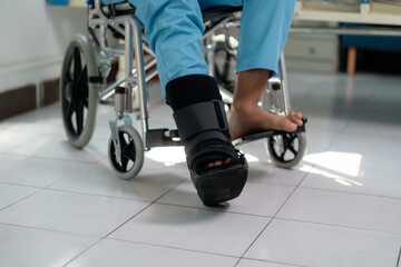 Patient recovering in wheelchair, wearing medical walking boot, resting in hospital room during...