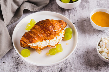 Croissant with ricotta, grapes and honey on a plate on a table