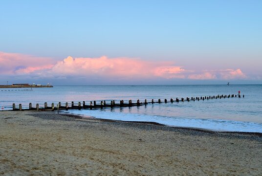 A sunset view of the North Sea with a groyne protecting the beach from erosion at the seaside resort of Lowestoft, with pink clouds on the horizon and a blue sky at dusk, England. 