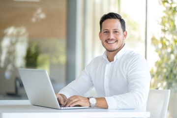 Fototapeta premium Smiling man works on a laptop in a bright, modern office, ready to tackle the challenges
