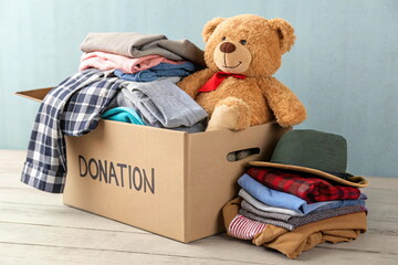 Donation box with clothes and teddy bear on floor in room. Charitable donation box. Helping low-income families, trash pickup, garage sale