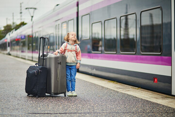 girl on a railway station. Little child waiting for a train on a platform. Kid with a luggage ready...