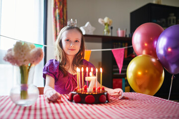 Happy little girl celebrating her seventh birthday and making a wish. Little kid with birthday cake...