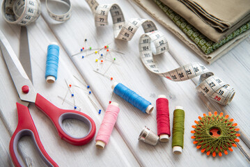 Sewing utensils - colored spools of thread, fabrics, tape measure and thimble on wood