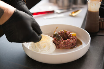 Chef preparing meat, Beef tartare with capers, raw egg, whipped cream cheese, gourmet dish