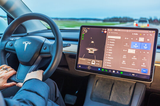 Close up view of Tesla Model Y driver holding steering wheel while using autopilot and control settings on touchscreen. Sweden. 