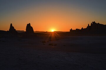 Sunset over rock formations in a desert landscape with silhouettes and a warm glow