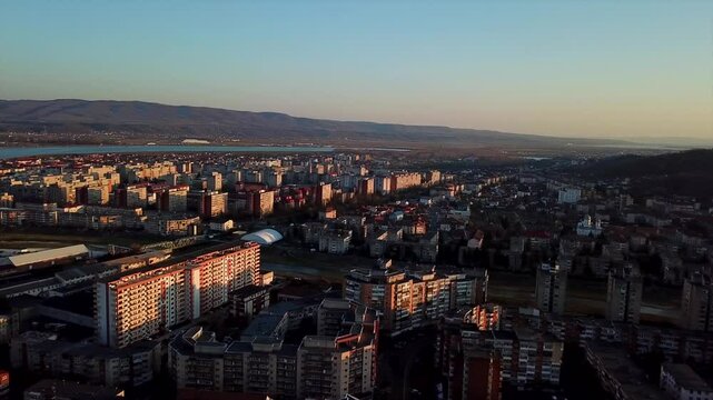 Drone shot of the sunset in Ramnicu Valcea, Romania,  showcasing its cityscape, hills, and river