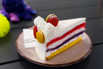Close-up of a colorful layered cake with macarons on top, served on a plate in a cozy cafe.