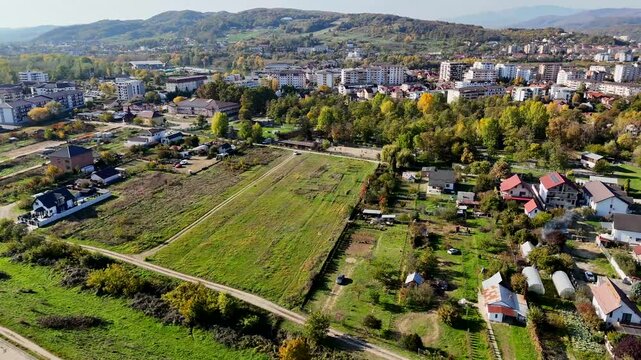 Aerial drone view of rural cityscape houses, trees and green fields in Ramnicu Valcea city, Romania