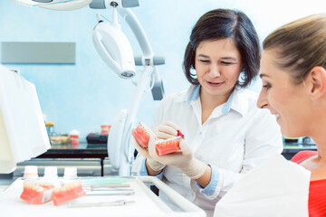 Professional female dentist doctor smiling and showing denture with braces to her patient in clinic