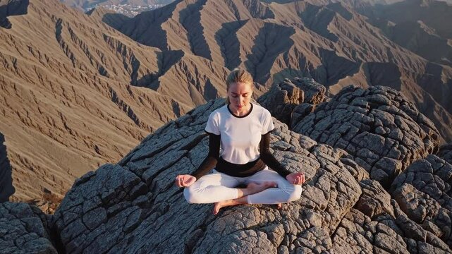Overhead shot of a young woman meditating on the top of a rock in the mountain.