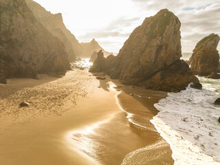 Dramatic coastal landscape featuring towering rock formations, golden sand, and ocean waves crashing against the shore under a warm sunset.  Stock photo © Timur Abasov