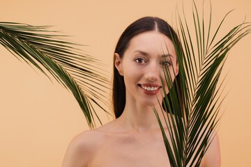 Naklejka premium Beautiful smiling woman posing with palm leaves on beige background
