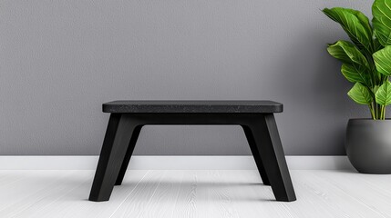 Modern black stool against a minimalistic gray wall with green plant.