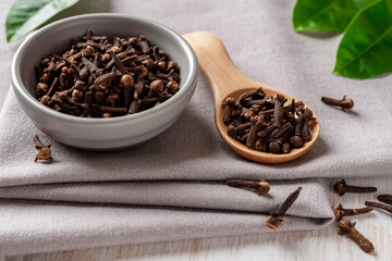 Bowl of organic clove buds close-up. Dry whole cloves spice in a small gray bowl and light wooden spoon over gray textile background. Spice and condiment concept.