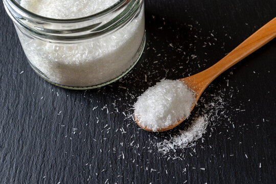 Monosodium glutamate in a wooden spoon and glass jar full of MSG white crystals over black background. Concept of food additive flavor enhancer E621.