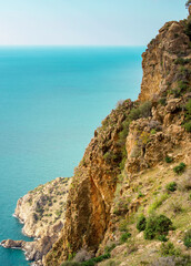 Rocky cliff overlooks the ocean, with a clear blue sky in the background