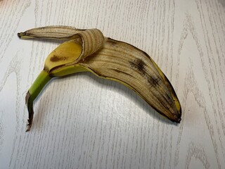 A banana peel lies on a light-colored wooden surface, displaying its yellow-brown hue and...