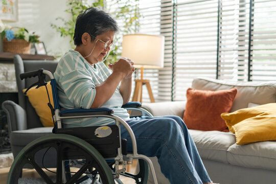 asian senior retired woman sitting on wheel chair in living room at home.Sad or depressed Elderly female in a wheelchair looking through window,asian senior retired woman alone at home,after retirment