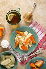 Lazy dumplings of cottage cheese with sour cream and persimmons and peanut butter and a cup of tea on mocha color table. Summer vegan Breakfast