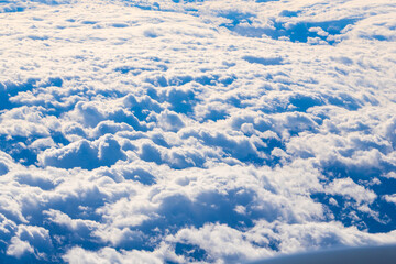 Soft white clouds blanket the sky during a bright midday flight over scenic landscapes