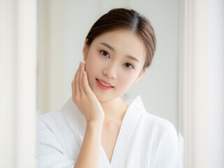 A young woman in a white robe gently touching her face, showcasing a fresh and radiant complexion, symbolizing skincare, beauty, and self-care.
