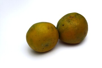 Two tangerines with a distinctive yellow-green rind sit on a white surface