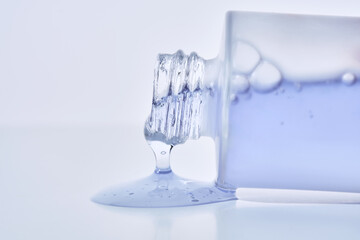 A cosmetic bottle from which a blue emulsion is poured.