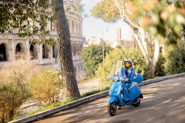 Plakat A fashionable woman in a blue outfit and helmet rides a scooter near the iconic Colosseum in Rome, Italy. The image captures the essence of Italian lifestyle, freedom, and elegance on two wheels