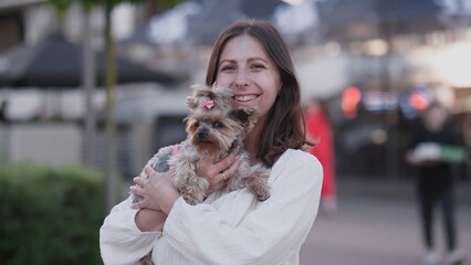 A joyful woman happily embraces her small, adorable dog in a vibrant and lively urban environment...