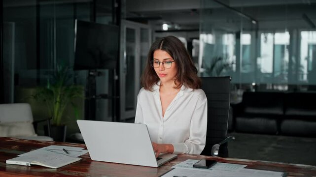 Focused young businesswoman professional it specialist using pc doing online banking analysing at workplace. Latin hispanic middle age business woman working on laptop computer AI app in modern office