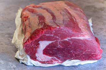 A whole, fresh, raw beef ribeye joint sits, with details showing a fat marble on the juicy face of the steak.